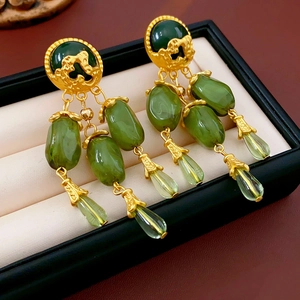 Detailed macro view of vintage gold tassel earrings with olive green gems in a jewelry box