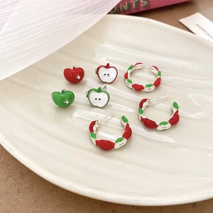 Detail view of red and green enamel apple stud earrings and silver-tone hoops on ceramic