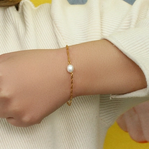 Vista macro di un bracciale a corda dorata con una singola perla bianca tonda