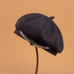 Close-up of black beret featuring a silver metal chain and engraved Paris triangle tag