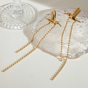 Golden hummingbird tassel earrings with long spherical chains on a minimalist background