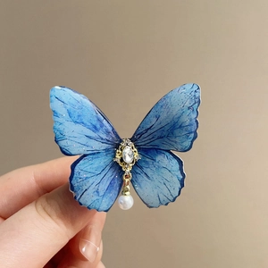 Detail of blue butterfly hair clip with gold frame, crystal center, and pearl pendant