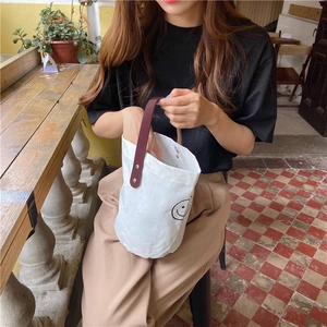 Close-up of white canvas bucket bag with smiling face print and red leather handle