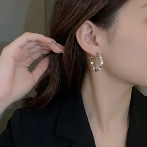 Elegant C-shaped silver stud earrings with small pearls and metal discs on a female model