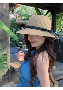 Detail of wide brim straw hat featuring an elegant black ribbon bow in a tropical outdoor setting