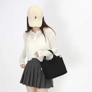 Casual lifestyle shot of a spacious black canvas tote bag paired with a pleated mini skirt