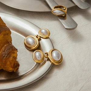 Macro view of gold vintage pearl earrings and ring on a stainless steel platter