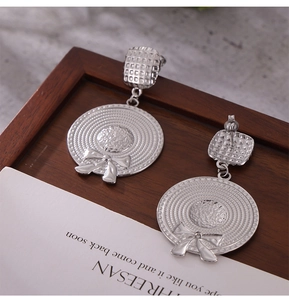 Detailed view of silver bow-knot sun hat earrings displayed on a dark wooden tray