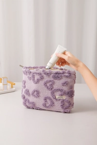 Close-up of purple plush makeup bag with 3D heart pattern being filled with hand cream