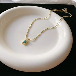 Detail of bohemian gold chain necklace featuring small green beads and turquoise pendant