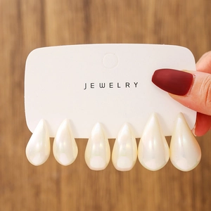 Detail view of six teardrop pearl acrylic stud earrings on a white jewelry display card