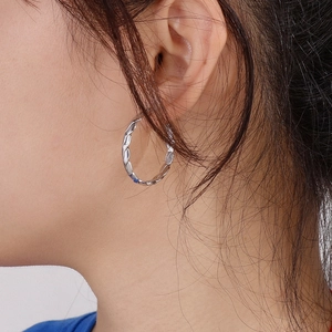 Close-up of a model wearing silver twisted hoop earrings made of titanium steel