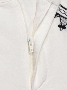 Close-up of white cotton linen fabric with black embroidery and metal zipper detail