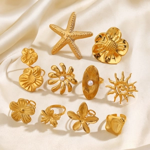 Goldenes Edelstahl-Ring-Set mit Sonne, Blumen und Perlen auf beigem Seidenhintergrund