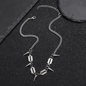 Detail of punk silver chain necklace featuring razor blade and cone spike charms