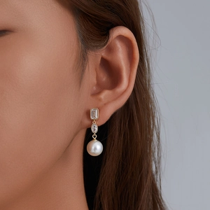 Elegant gold earrings with square zircon and white round pearls worn by a model