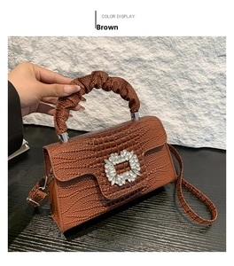 Detail of brown crocodile pattern handbag with rhinestone buckle and pleated handle