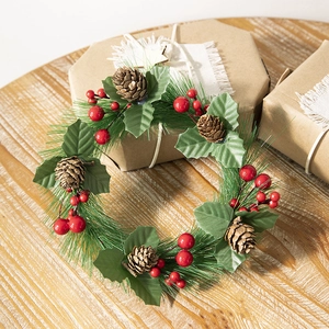Christmas wreath with green pine needles, brown cones, and red berries on a gift box