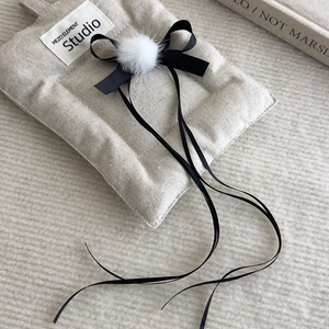 Close-up of ballet-style linen hair clip featuring black bow and white fur pom-poms