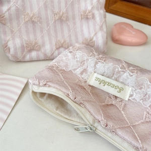 Detailed texture of pink satin makeup bag with floral embroidery and white lace trim