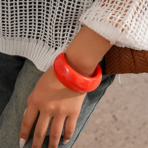 Close-up of a wide red resin bangle on a woman's wrist with knitwear and woven bag