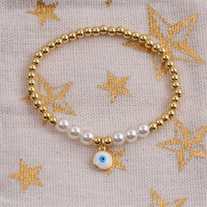 Bracelet à perles dorées avec perles blanches et charm œil bleu sur un fond étoilé