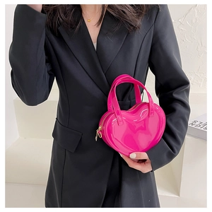 Close-up of heart-shaped mini handbag in glossy pink leather held by a model