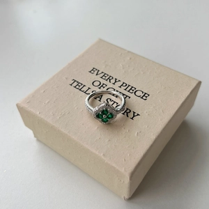 Macro shot of silver four-leaf clover ring with green zircons on a textured gift box