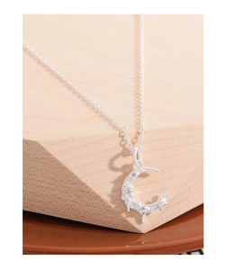 Macro detail of silver crescent moon pendant with sparkling zircons on wooden block