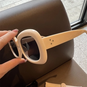 Details einer Oversize-Sonnenbrille in Creme mit Metallnieten und dunklen Gläsern