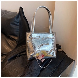 Close-up of silver metallic pleated handbag with bow accents and bead chain strap detail