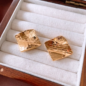Close-up of 18k gold plated square stud earrings with hammered texture in a wooden box