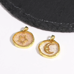 Golden star and moon pendants with pink glitter inlay on a stone slab background