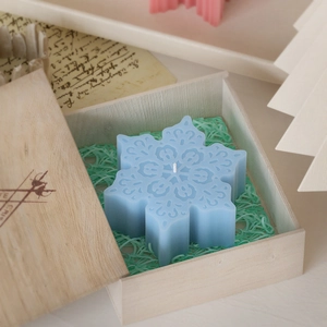 Detail van een lichtblauwe geurkaars in sneeuwvlokvorm in een houten geschenkdoos