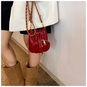 Close-up of red camellia drawstring bucket bag with gold chain strap worn by a person