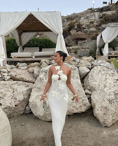 Detail of white hollow crochet knit dress with 3D floral accents on a beach backdrop