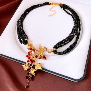 Detail of multi-layer black beaded necklace with golden vine pendant and red berries