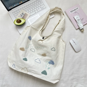 Detail shot of cloud embroidery and metal button closure on white canvas tote bag