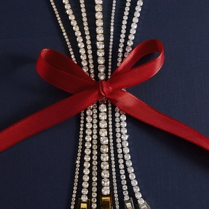 Dettaglio di bracciali tennis in argento e oro con zirconi su sfondo blu e nastro rosso