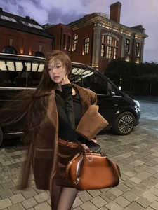 Detail of brown velvet blazer styled with a leather handbag against a vintage brick wall