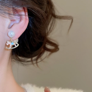 Macro side view of silver needle pearl earrings with pink and blue rocking horse charms