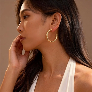 Detail view of large gold twisted hoop earrings with geometric texture on a model