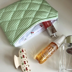 Detail of green checkered quilted makeup bag with cherry print lining and hair claw clip