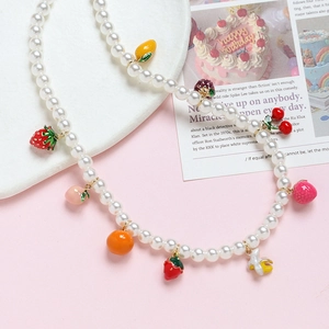 Detail of pearl necklace featuring colorful strawberry and orange fruit charms