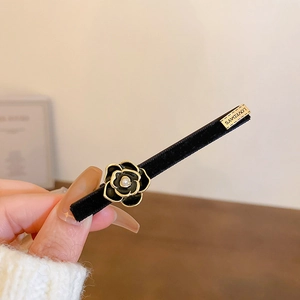 Detail of velvet camellia hair clip with pearl center and engraved gold label