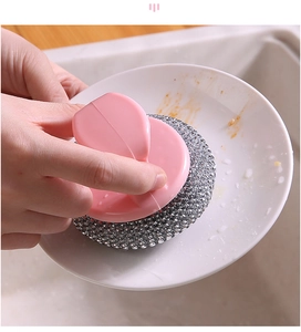Pink ergonomic handle steel wire brush cleaning a stained white ceramic plate in a sink