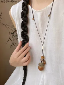 Detail of acorn pendant on brown woven rope worn with white linen clothing