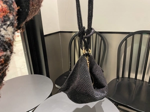 Detail of a black rhinestone triangle handbag with a knotted handle and gold zipper