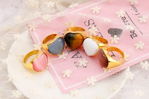 Macro view of five colorful heart-shaped gemstone rings with gold-plated bands on lace