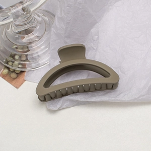 Macro detail of a large matte khaki hair claw clip resting on white textured paper